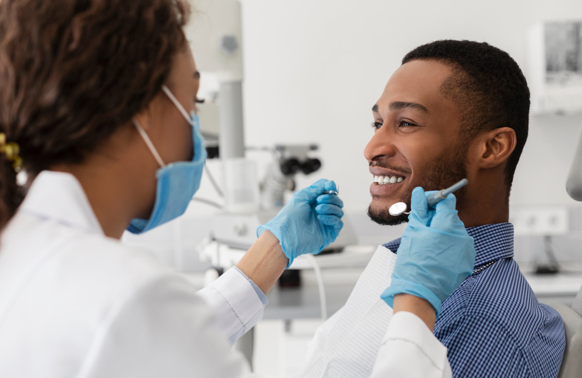Young, black man smiling to his female dental hygienist while having treatment at modern clinic